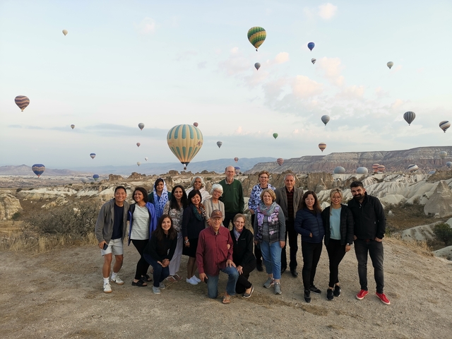 Group of people with hot air balloons in the backdrop.