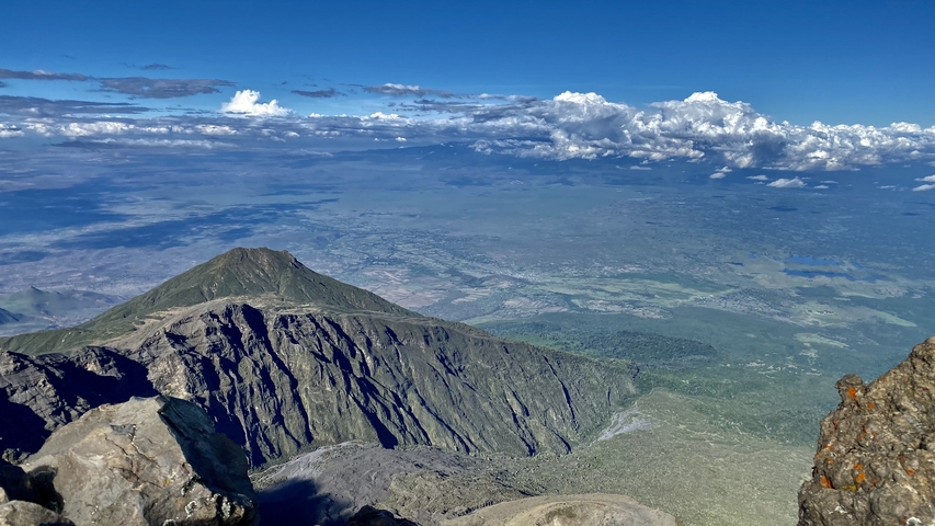       Aerial view over a dramatic landscape with clouds and mountains.
  