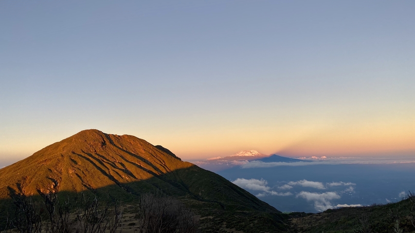       Mountain with a vibrant sunset and a layer of clouds below.
  