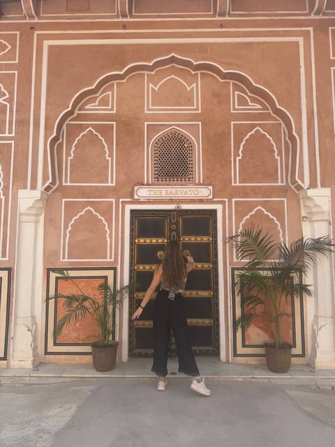 Person posing against a decorative wall with geometric pattern.