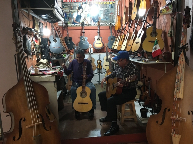       Two men playing guitars surrounded by instruments.
  