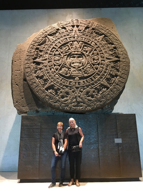       Two women in front of the Aztec Sun Stone.
  