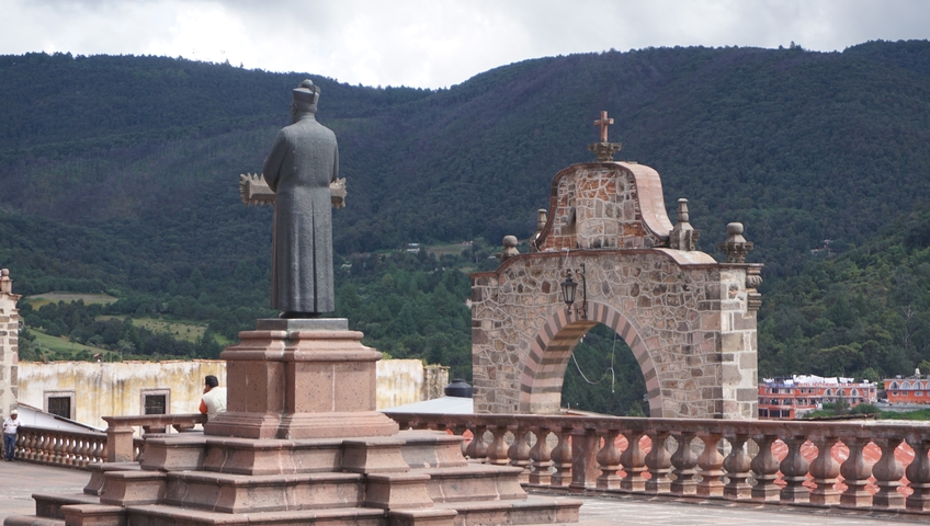       Statue and arch with mountains in the background.
  