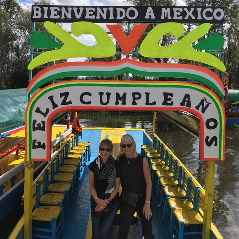       Two women under a colorful 'Feliz Cumpleaños' sign on a boat.
  