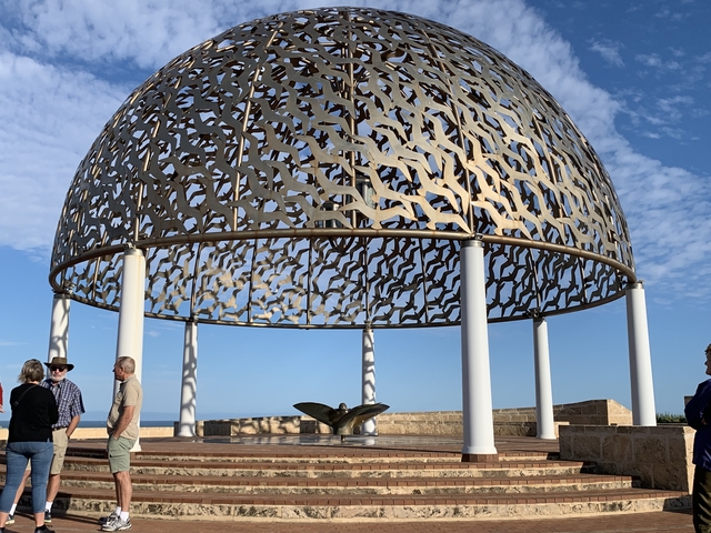 A group of people under a decorative dome structure overlooking the ocean.
