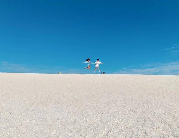 Two people jumping in the air on a white sandy beach.