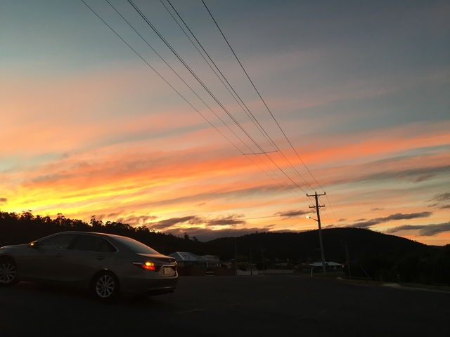 A parked car against a colorful sunset over hills.