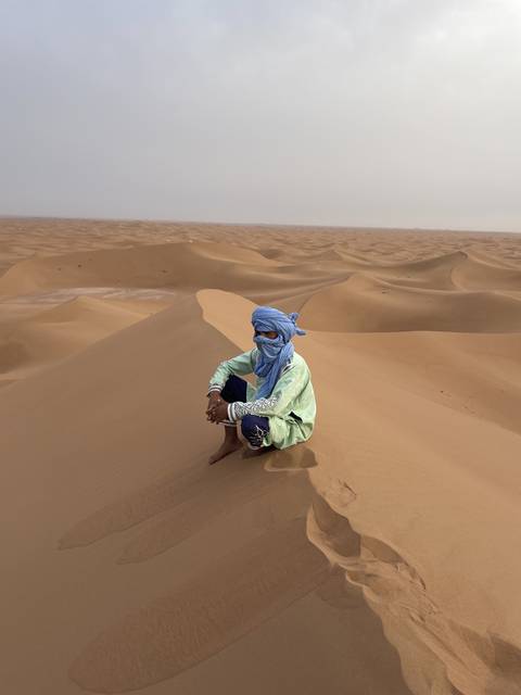 A person wearing traditional clothing on sand dunes.