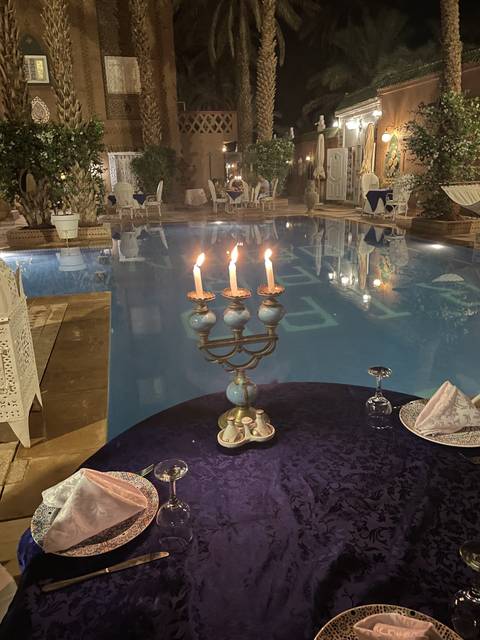 An outdoor dining area by a pool with candlelights at night.