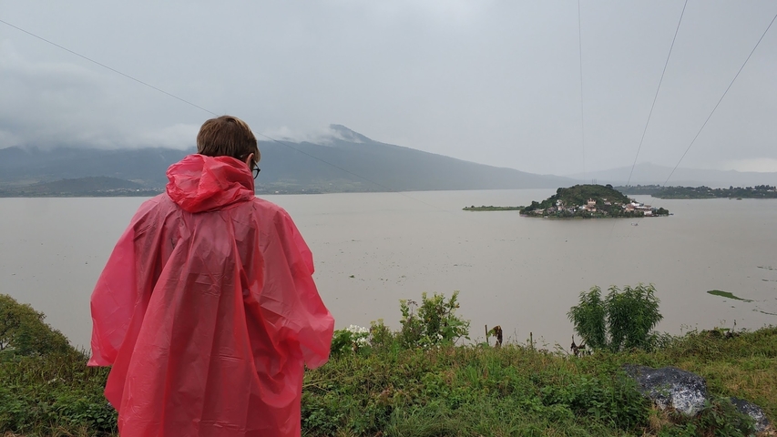       Person in red raincoat overlooking a lake and island
  