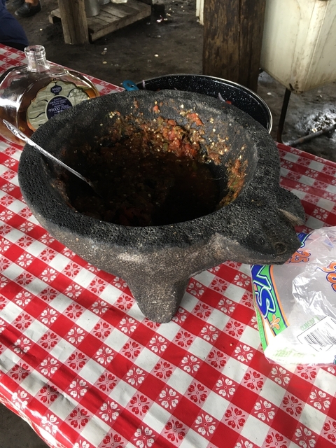       A molcajete with salsa on a red and white checkered tablecloth
  