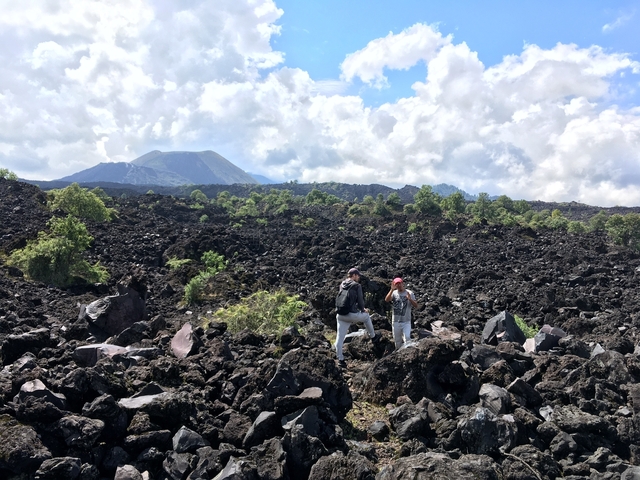       Two people observing a volcanic landscape with mountains.
  
