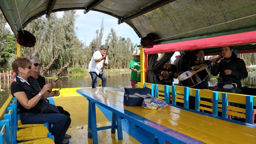       People on a boat with musicians, trees in the background
  