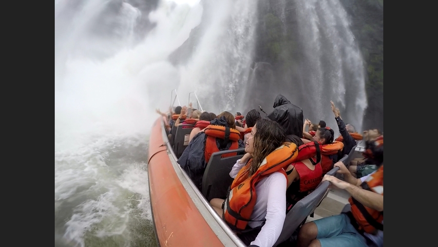 Tourists in a boat approaching a waterfall.