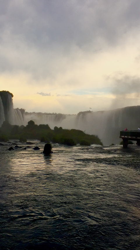 Distant view of Iguazu Falls with people on a viewing platform.