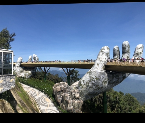 Golden Bridge held by giant stone hands with tourists walking.
