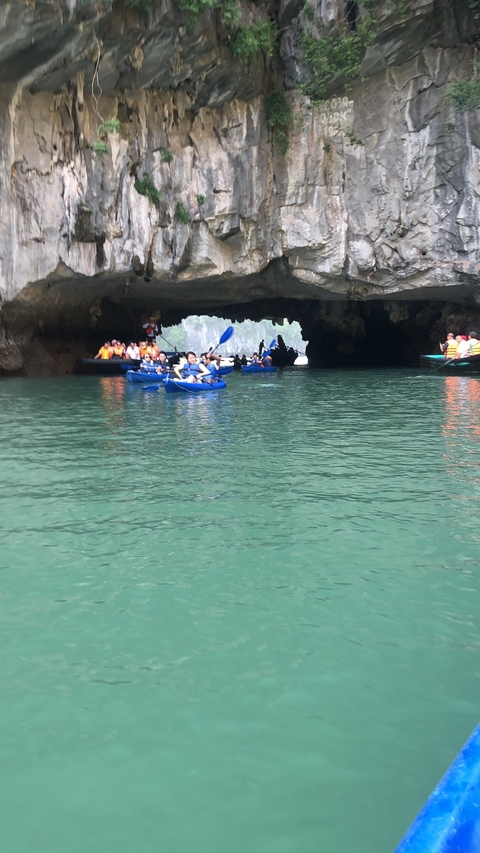 People kayaking inside a cave on calm green water.