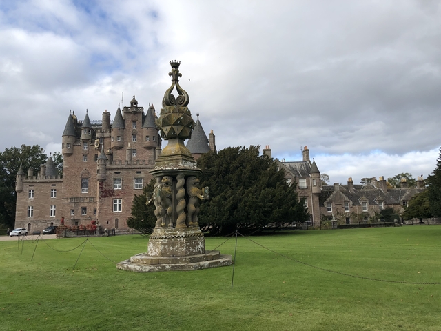       Historic castle with a decorative stone structure on green grounds.
  