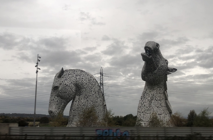       Large sculptures of horse heads with cloudy sky and utility poles.
  
