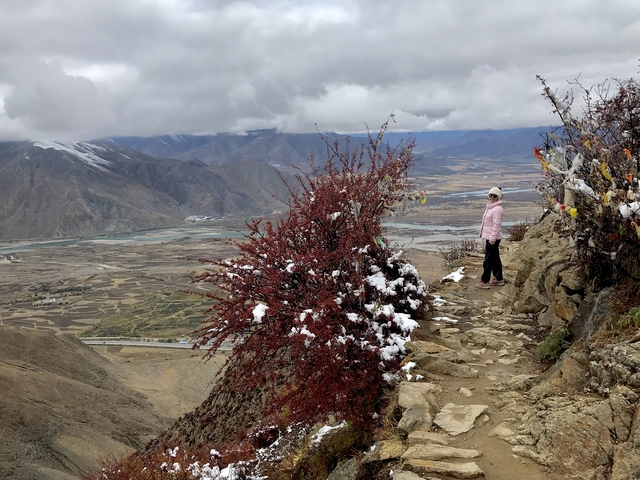 Person on a mountain trail with snow-covered peaks in the distance.