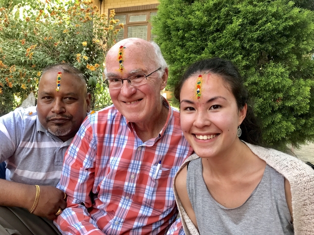 Three people with traditional forehead markings smiling outdoors.