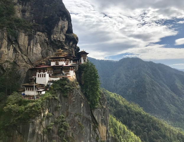 Monastery built into a cliffside with forested mountains.