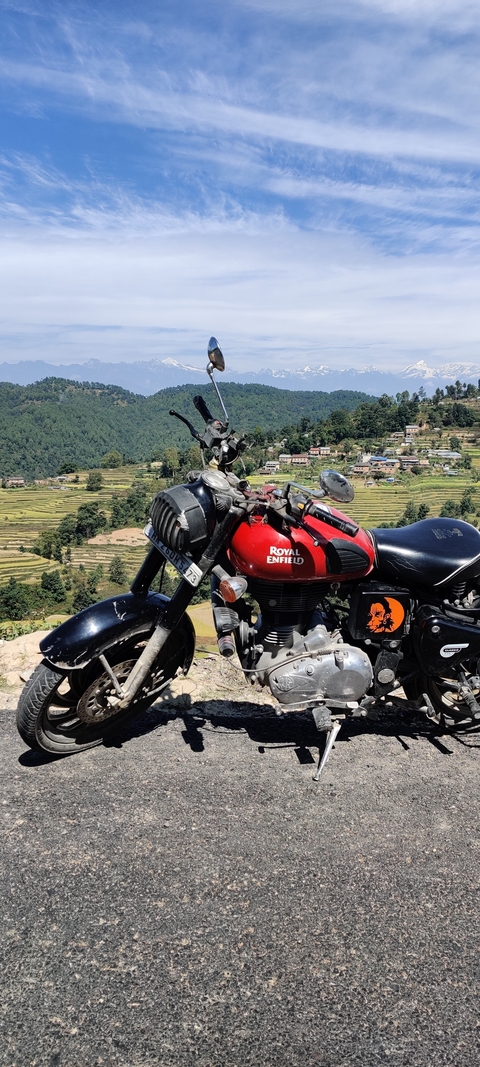       Red motorcycle with mountains and terraced fields in the background.
  