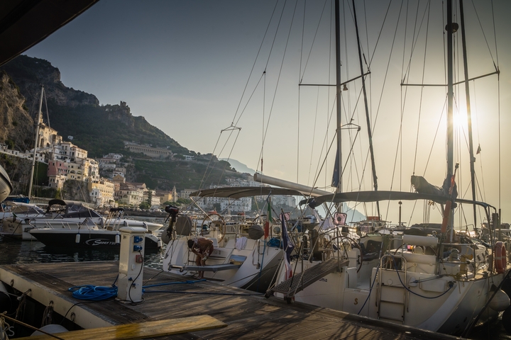 Boats docked at a marina with hillside buildings.