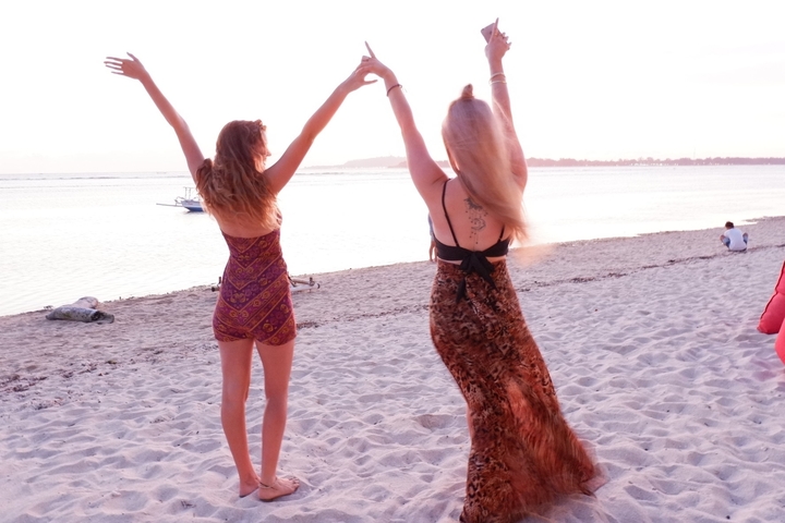 Two people dancing joyfully on a beach at sunset.