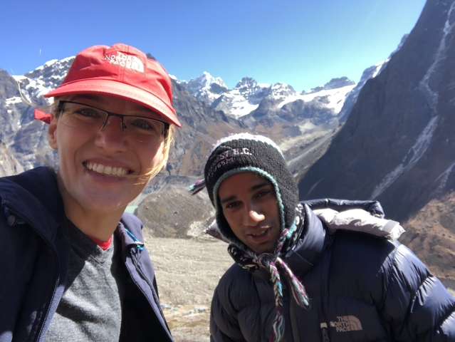 Two hikers in winter gear smiling with snowy mountains behind them.
