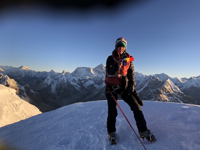 Hiker on a snowy peak with a view of other mountain ranges.