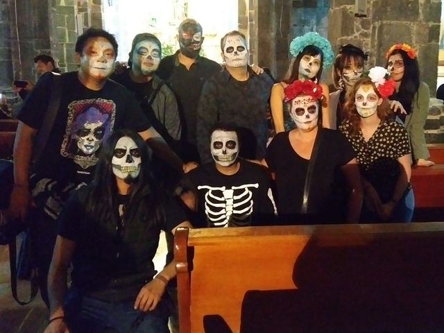       A group of people with faces painted like skulls in a dimly lit room.
  