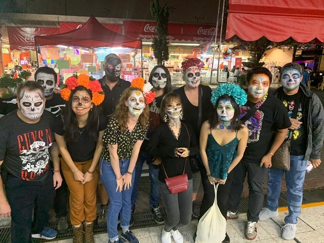       Group of people with face paint and flowers celebrating Day of the Dead.
  