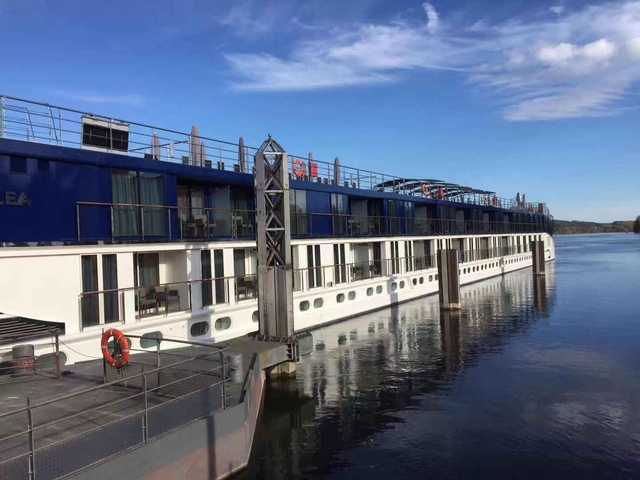River cruise ship docked by the shore under blue sky.