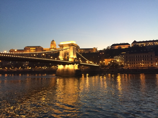 Night view of a lit suspension bridge and city lights reflecting on water.