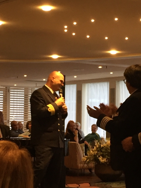 Person holding a microphone speaking to a crowd indoors.