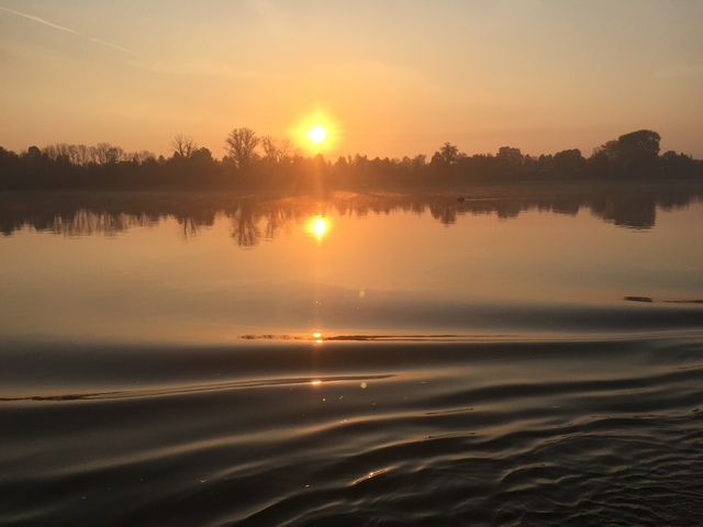 Sunset over a calm body of water, reflecting the sun.