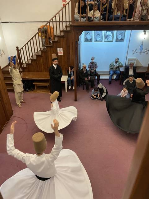 Whirling dervishes performing inside a room with spectators.