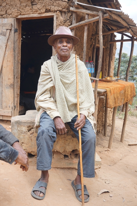       Elderly man sitting outside a rustic building.
  