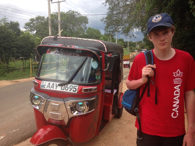       Person in red shirt standing next to a tuk-tuk on a road.
  