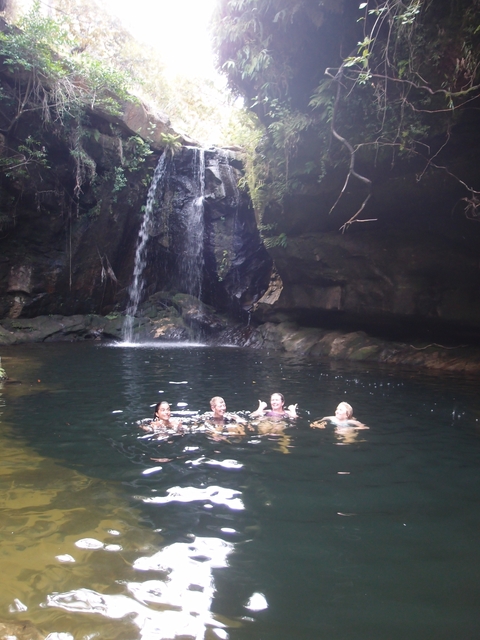 People swimming in a natural pool under a waterfall.