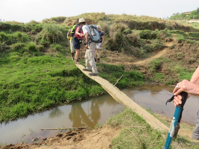       Hikers crossing a narrow plank over a creek.
  