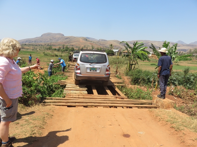 People standing by a wooden bridge while a car crosses it.