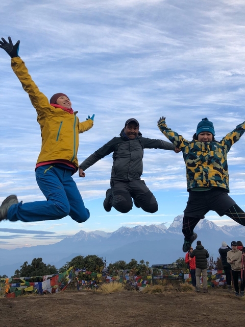       Three people mid-jump with mountains in the background.
  