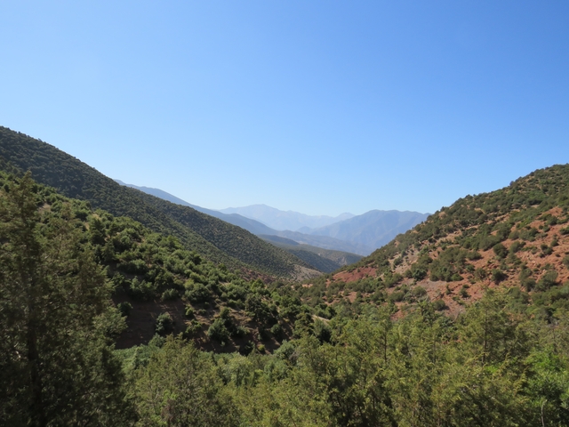 A scenic landscape view of lush green valleys and distant mountains under a clear blue sky.