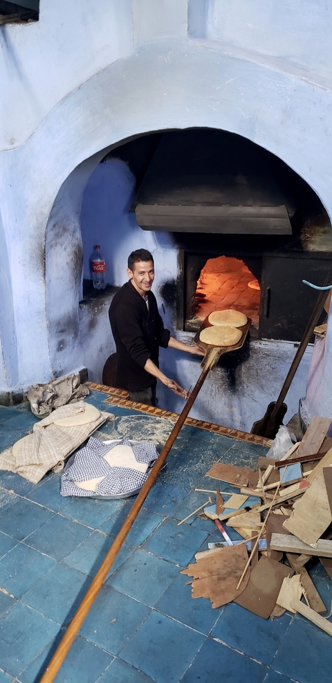       A man baking bread in a traditional oven.
  