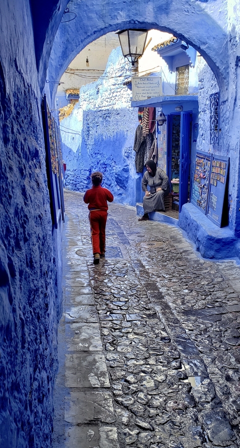       A child walking in a narrow blue-painted street.
  