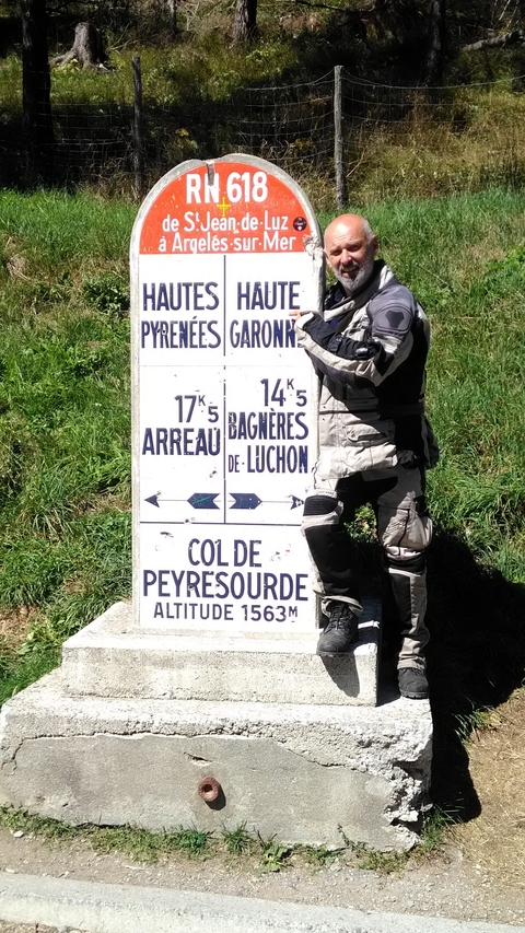       A motorcyclist pointing at a road sign for Col de Peyresourde.
  