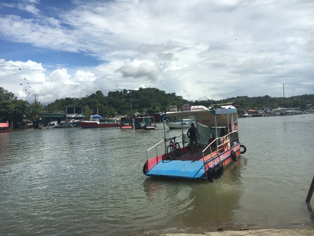 Small ferry boat in a harbor with hills in the background.