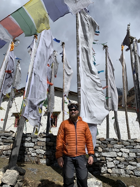 Man in front of prayer flags and mountains.